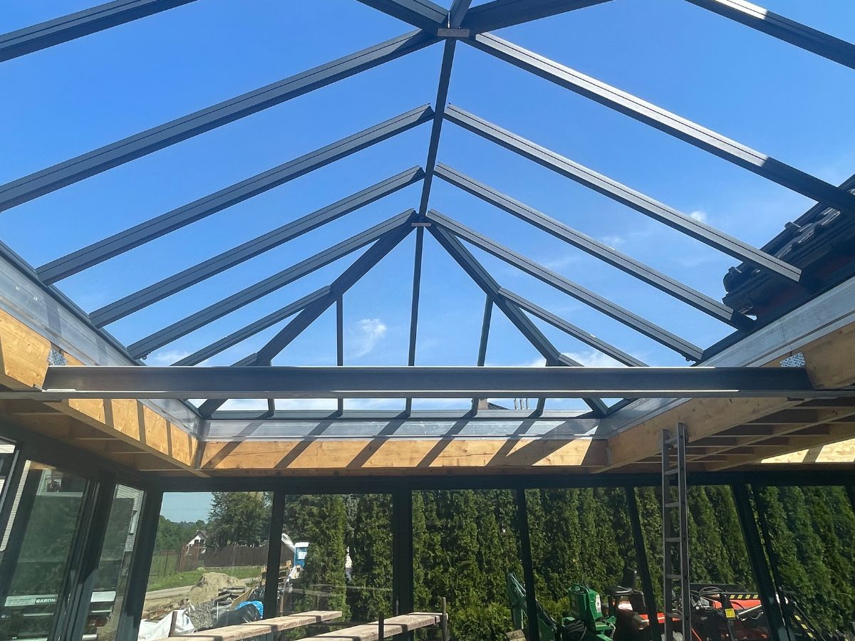 Realizacja VERANDANA w trakcie montażu – widok na stalową konstrukcję świetlika kopertowego Flandria Victory osadzonego na belkach z drewna klejonego BSH. Połączenie stali, drewna i szkła dla maksymalnego doświetlenia wnętrza.